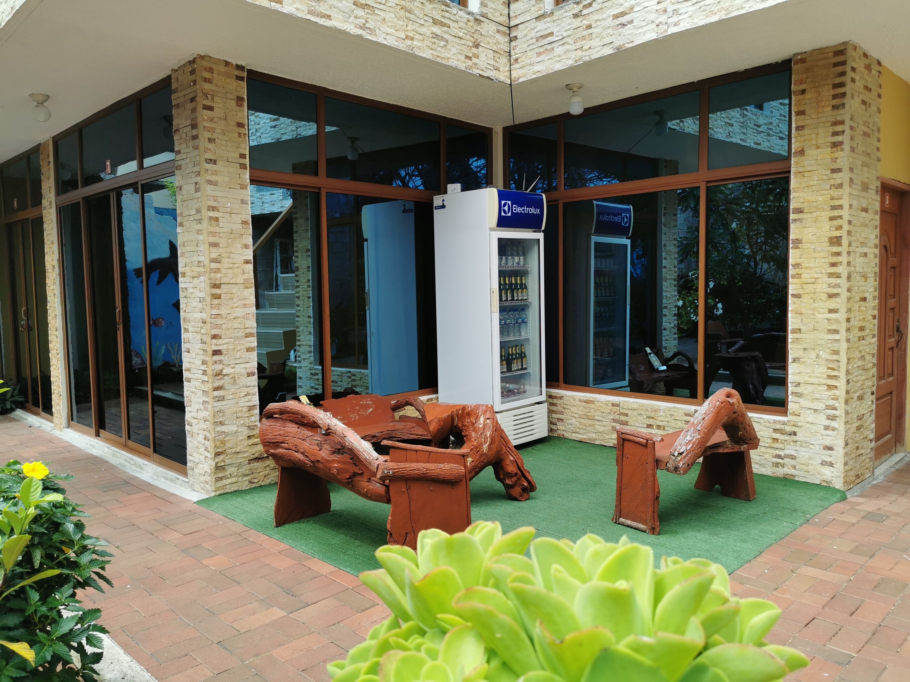A modern building with large glass windows, a brick exterior, and a seating area with wooden loungers.