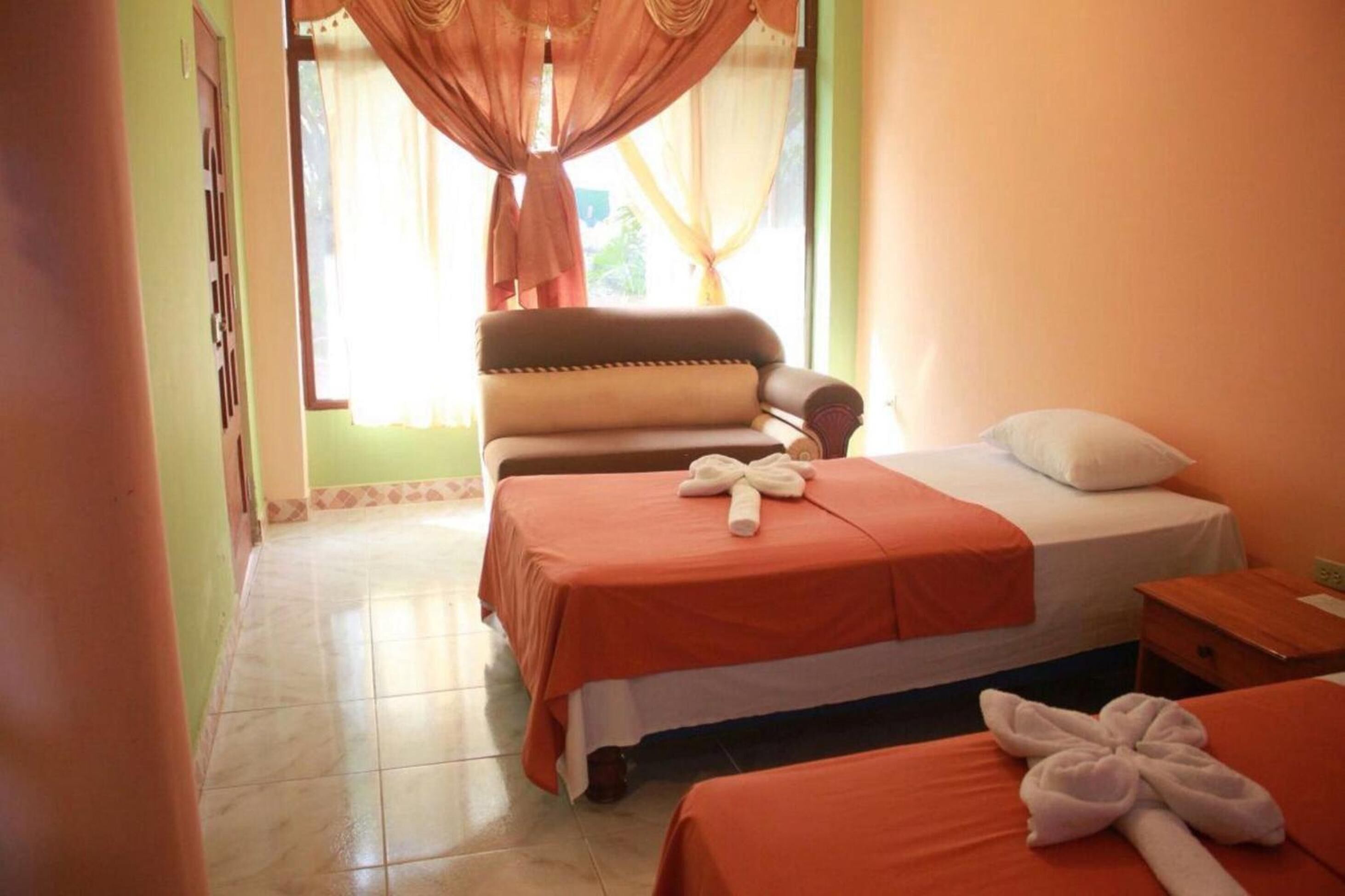 A hotel room with two beds, a sitting area, and a window with curtains.
