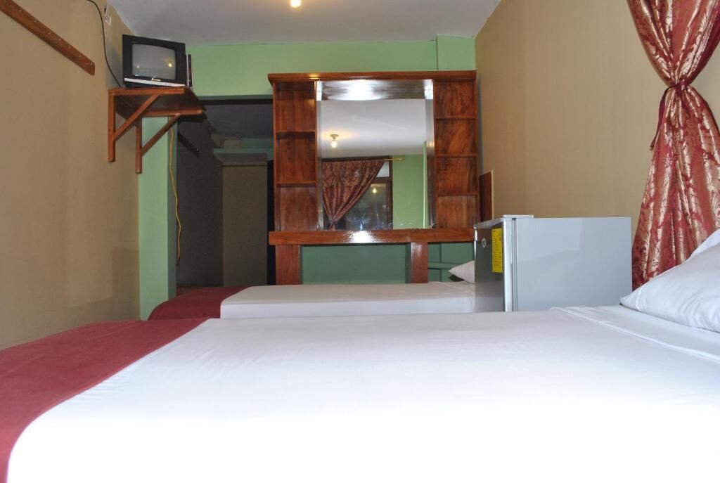 A room with a bed, a small television on a wooden stand, a mirror, and a red curtain.