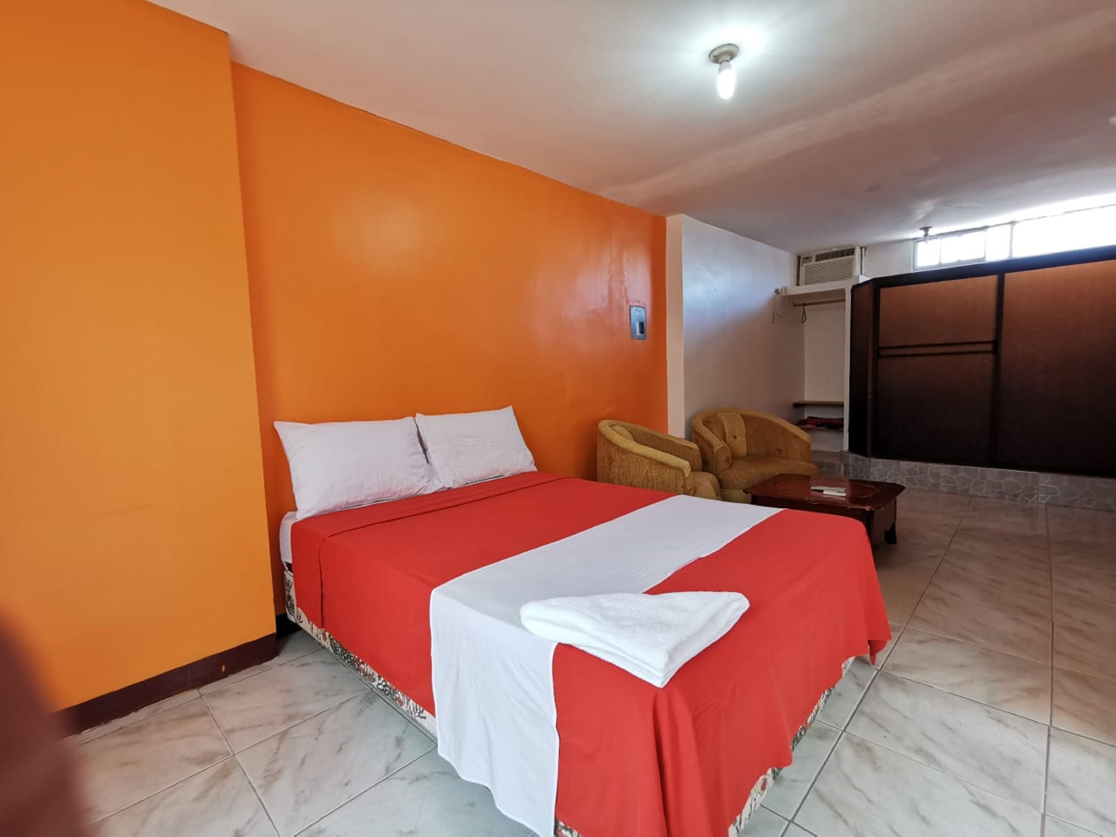 A hotel room with a bed, a chair, and a large window.