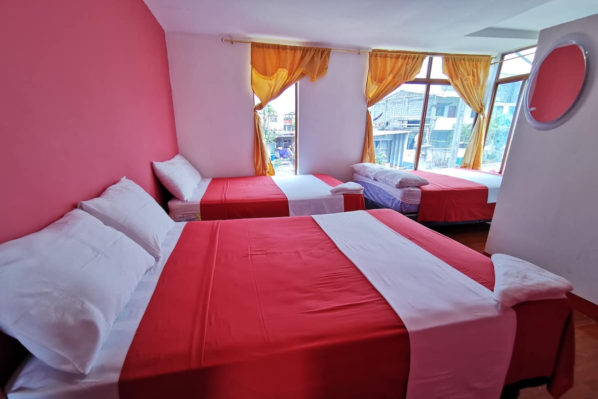 Habitación de hotel con dos camas, cada una con ropa de cama roja y blanca, y un ventanal con cortinas amarillas.