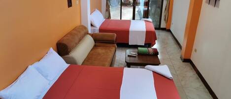 A hotel room with two beds, a sofa, a TV, and a sliding glass door to the outside.
