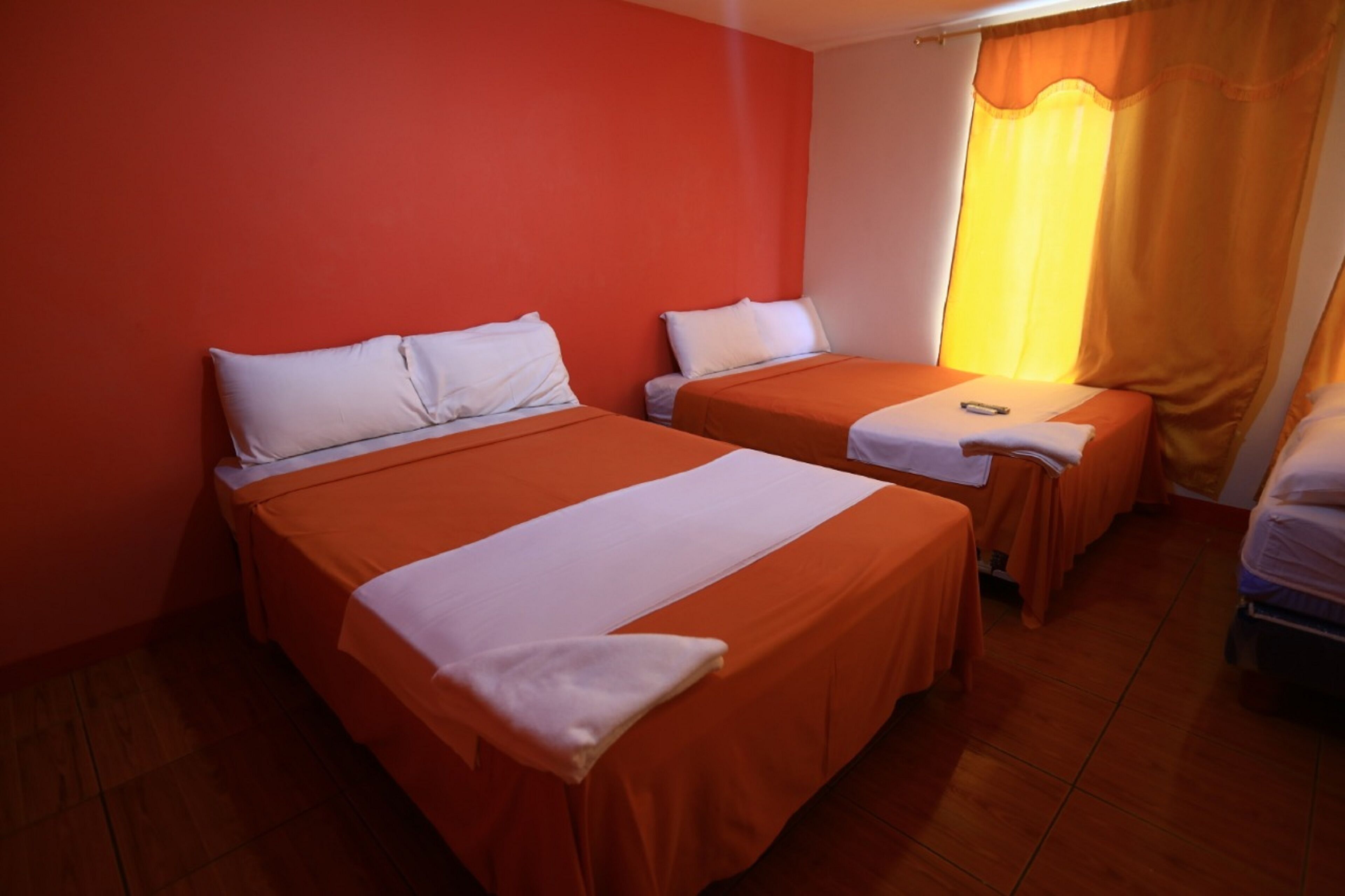 Quarto de hotel com duas camas de solteiro, cada uma com lençóis brancos e colchas laranja.