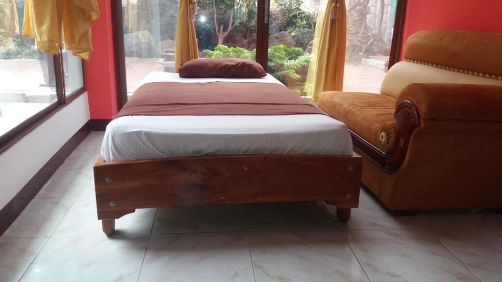 A bedroom with a wooden bed, a brown sofa, and a view of greenery outside.