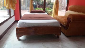 A bedroom with a wooden bed, a brown sofa, and a view of greenery outside.