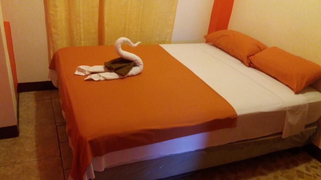 Een hotelkamer met een bed, oranje beddengoed, een handdoek in de vorm van een zwaan en oranje kussens.