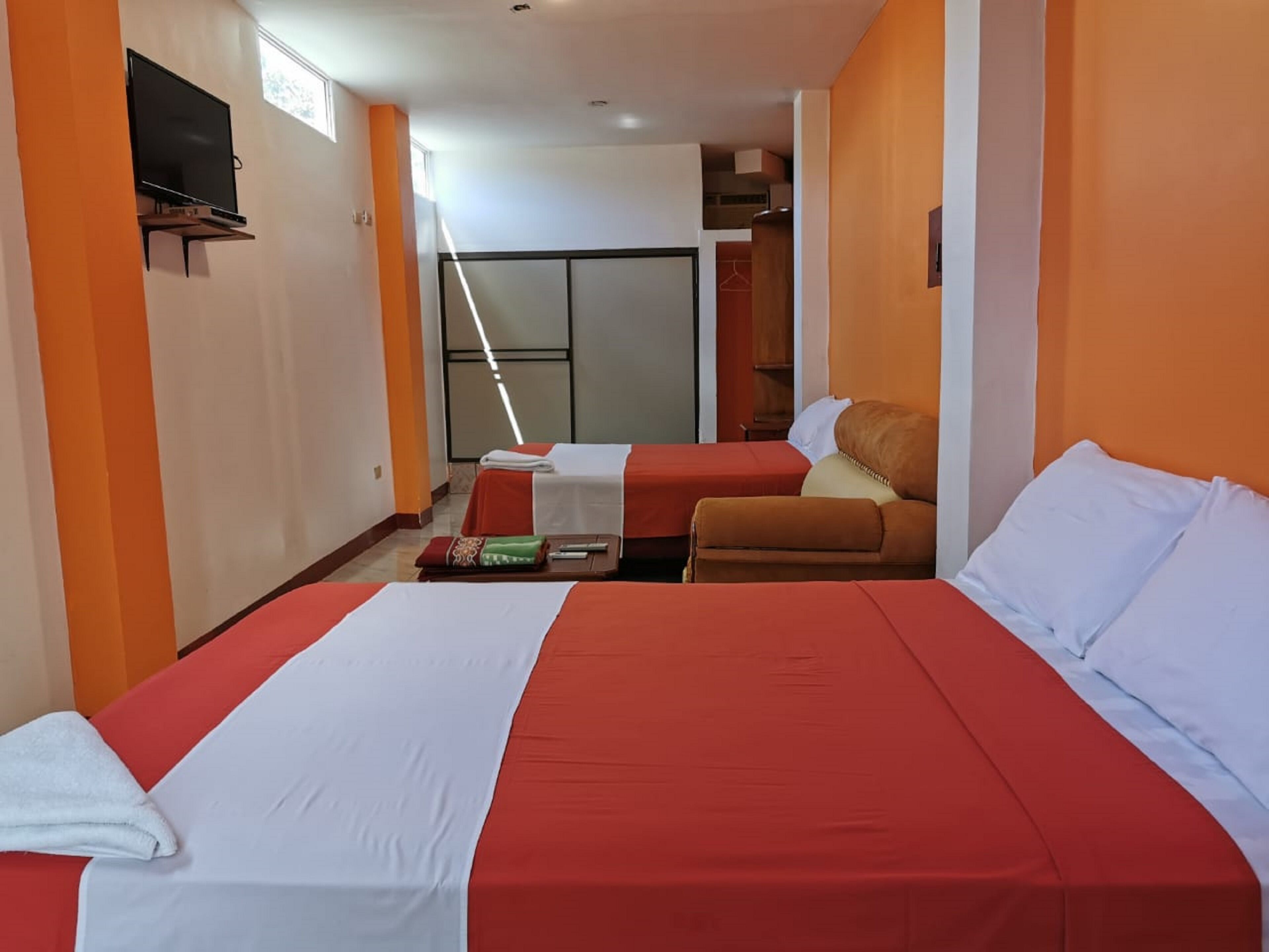 Ein Hotelzimmer mit zwei Betten, einem Fernseher und einer Schiebetür, die auf einen Balkon führt.