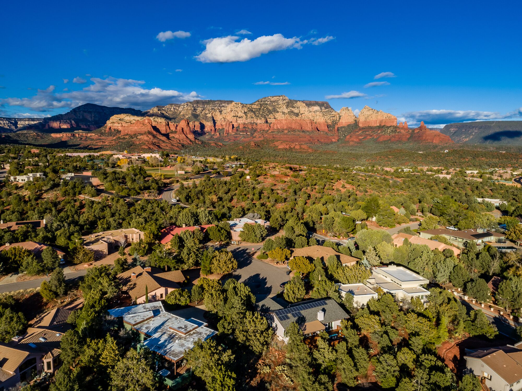 Une vue aérienne d’un quartier résidentiel, avec des maisons entourées d’arbres, le tout se détachant sur un paysage de formations rocheuses rouges.