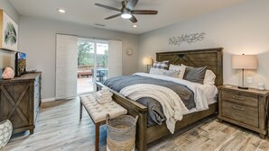 Un dormitorio con cama, mesitas de noche, un banco, ventilador de techo y vistas al exterior.