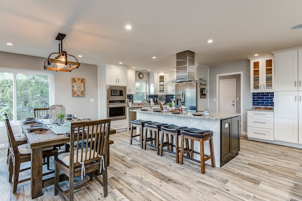 A modern kitchen with a central island, bar stools, and a dining area with a wooden table and chairs.