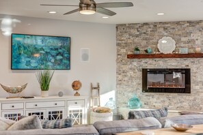 A modern living room with a stone fireplace, a large abstract painting, and a ceiling fan.