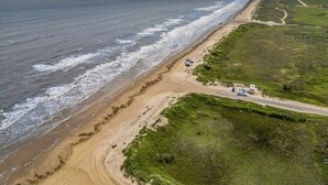 An aerial view of a beach with a road running parallel to the shore, a few vehicles, and some greenery. - The Sea Turtle, Family and Dog Friendly, Cargo Lift, Crystal Beach TX Ocean View (Bolivar Peninsula/Crystal Beach)