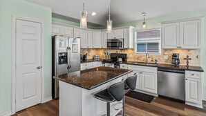 A modern kitchen with white cabinets, granite countertops, stainless steel appliances, and pendant lighting. - The Sea Turtle, Family and Dog Friendly, Cargo Lift, Crystal Beach TX Ocean View (Bolivar Peninsula/Crystal Beach)
