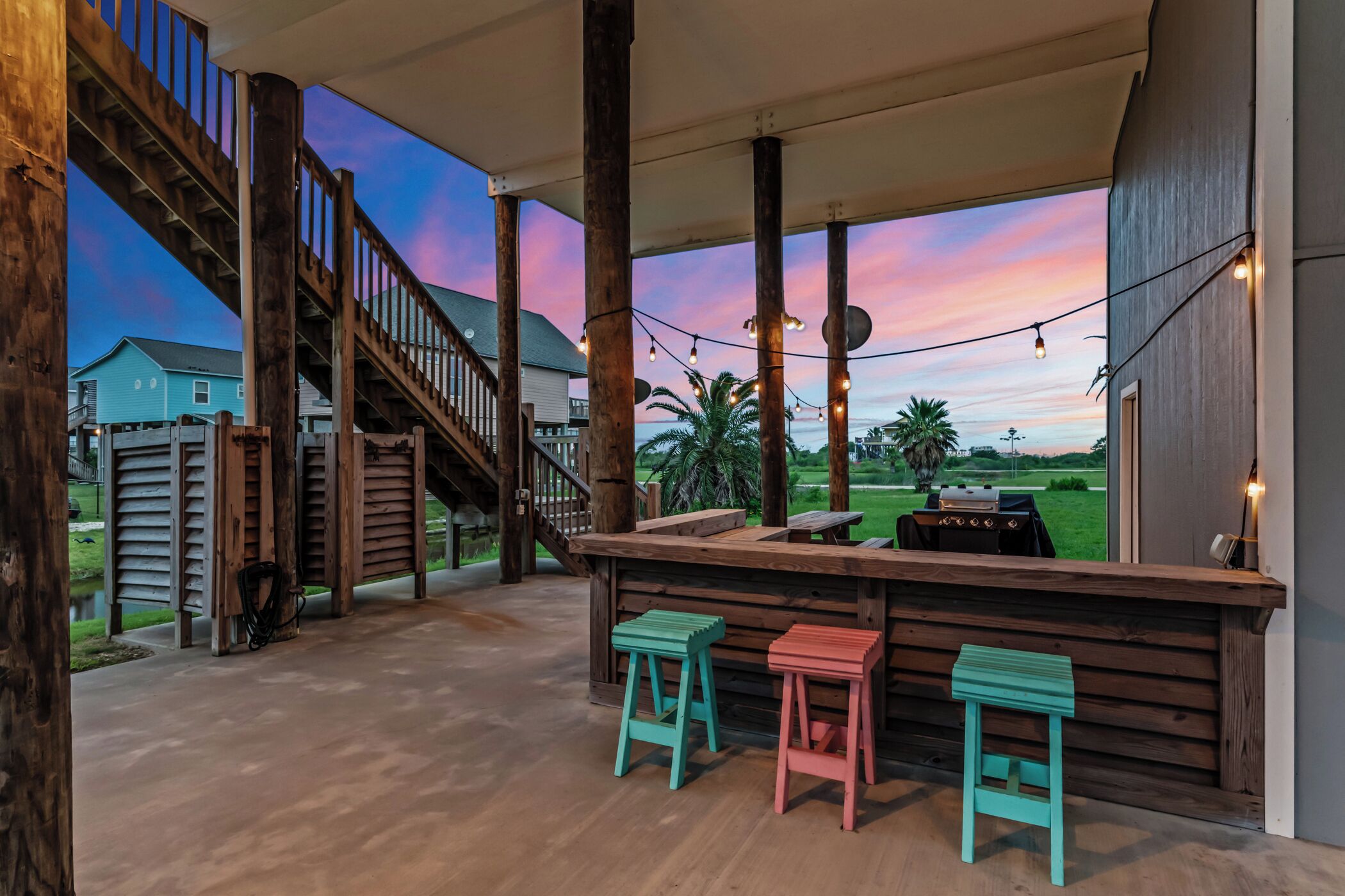 Une terrasse extérieure avec des poutres en bois, un escalier en bois et un coin bar avec des tabourets.