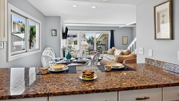 A modern kitchen with granite countertops, white cabinetry, and a dining area with a white table and chairs. - PRIME Resort Location! Beachside, Ocean View, Pool Access! (Isle Of Palms)