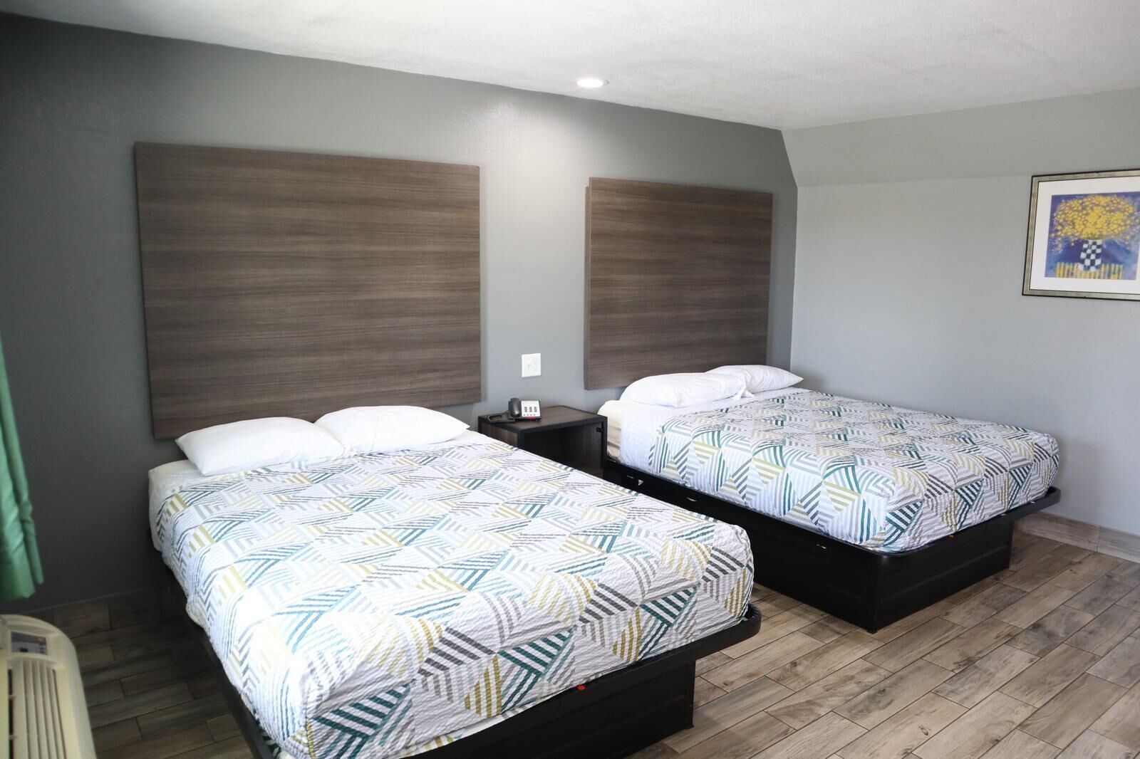 Une chambre d’hôtel avec deux lits, chacun agrémenté d’une literie à motifs, d’une table de chevet et d’un luminaire fixé au mur.