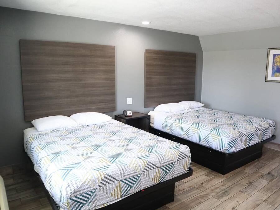 Une chambre d’hôtel avec deux lits, chacun agrémenté d’une literie à motifs, d’une table de chevet et d’un luminaire fixé au mur.