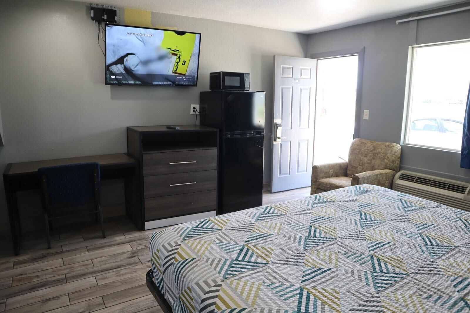 Quarto com cama, escrivaninha, cadeira, televisão e porta.
