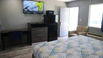 Quarto com cama, escrivaninha, cadeira, televisão e porta.