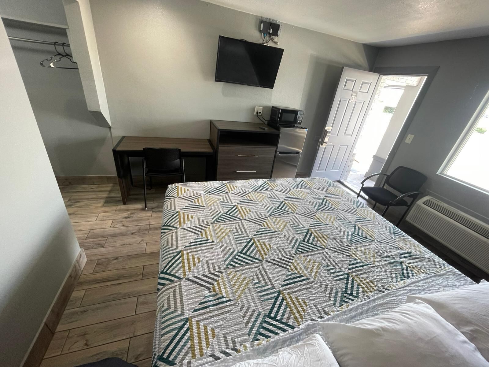 Un dormitorio con una cama, un escritorio, una silla, un televisor y una puerta.