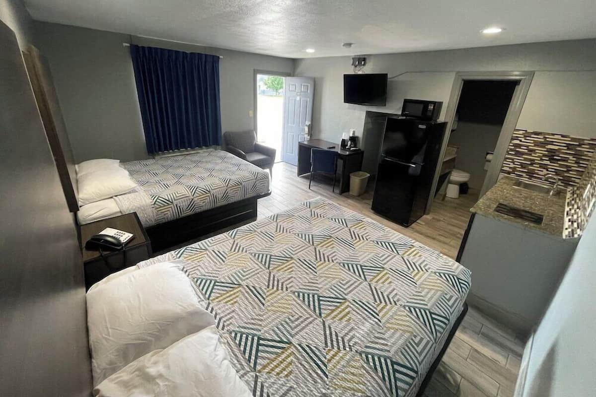 Quarto de hotel com duas camas, uma escrivaninha, televisão, frigorífico e banheiro.