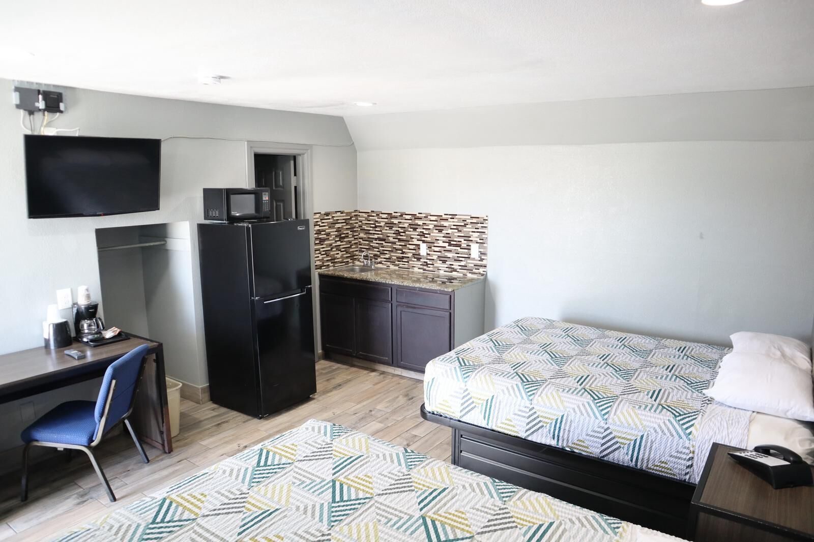 Habitación de hotel compacta con cama, escritorio, refrigerador, microondas, televisión y pared con estampado.