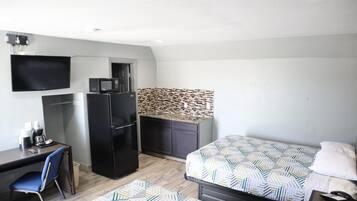 Habitación de hotel compacta con cama, escritorio, refrigerador, microondas, televisión y pared con estampado.