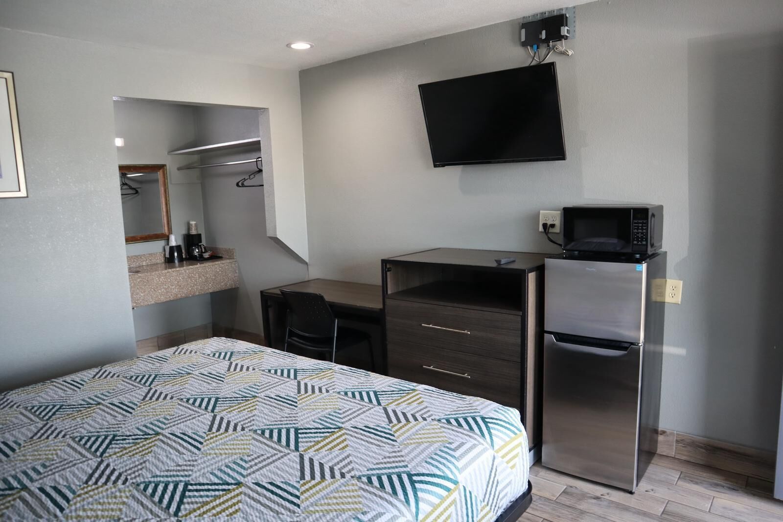 Habitación de hotel con cama, escritorio, silla, televisor de pantalla plana montado en la pared, microondas y refrigerador.