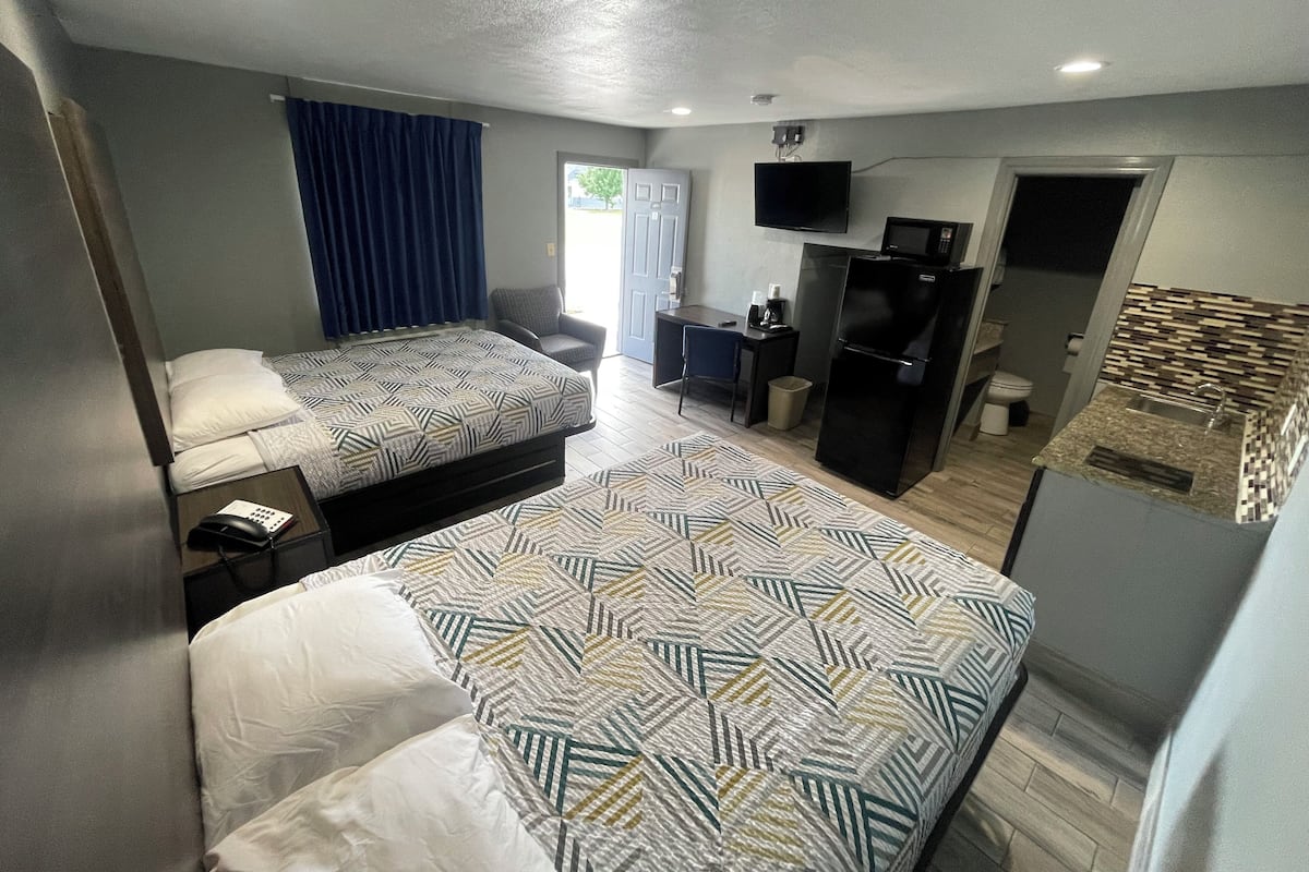 Quarto de hotel compacto com duas camas, uma escrivaninha, uma cadeira, uma televisão, um frigorífico e um micro-ondas.