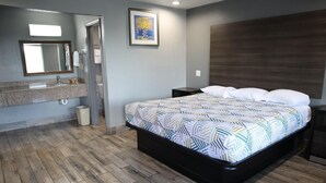 Een slaapkamer met een bed, nachtkastje, dressoir, spiegel en een schilderij aan de muur.