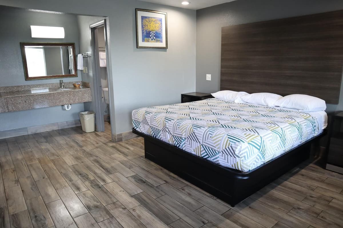 Quarto com cama, mesa de cabeceira, cômoda, espelho e um quadro na parede.