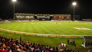 Un estadio con un campo amplio e iluminado, asientos para espectadores y algunas personas en el campo.