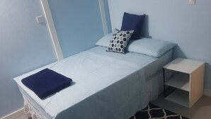 Habitación individual con decoración azul y blanca, una mesita de noche pequeña y una alfombra estampada.