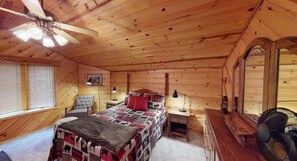 Una habitación acogedora tipo cabaña con una cama, un escritorio, una silla, un ventilador de techo y un espejo.
