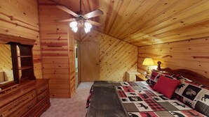 Een slaapkamer in een houten hutje, met een bed, een kapstok en een plafondventilator.