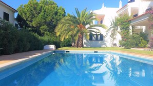 A swimming pool with clear blue water, surrounded by lush greenery and white buildings with red-tiled roofs.