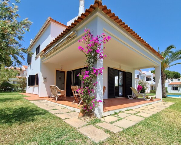 A two-story house with a covered patio, a small garden, and a pool.