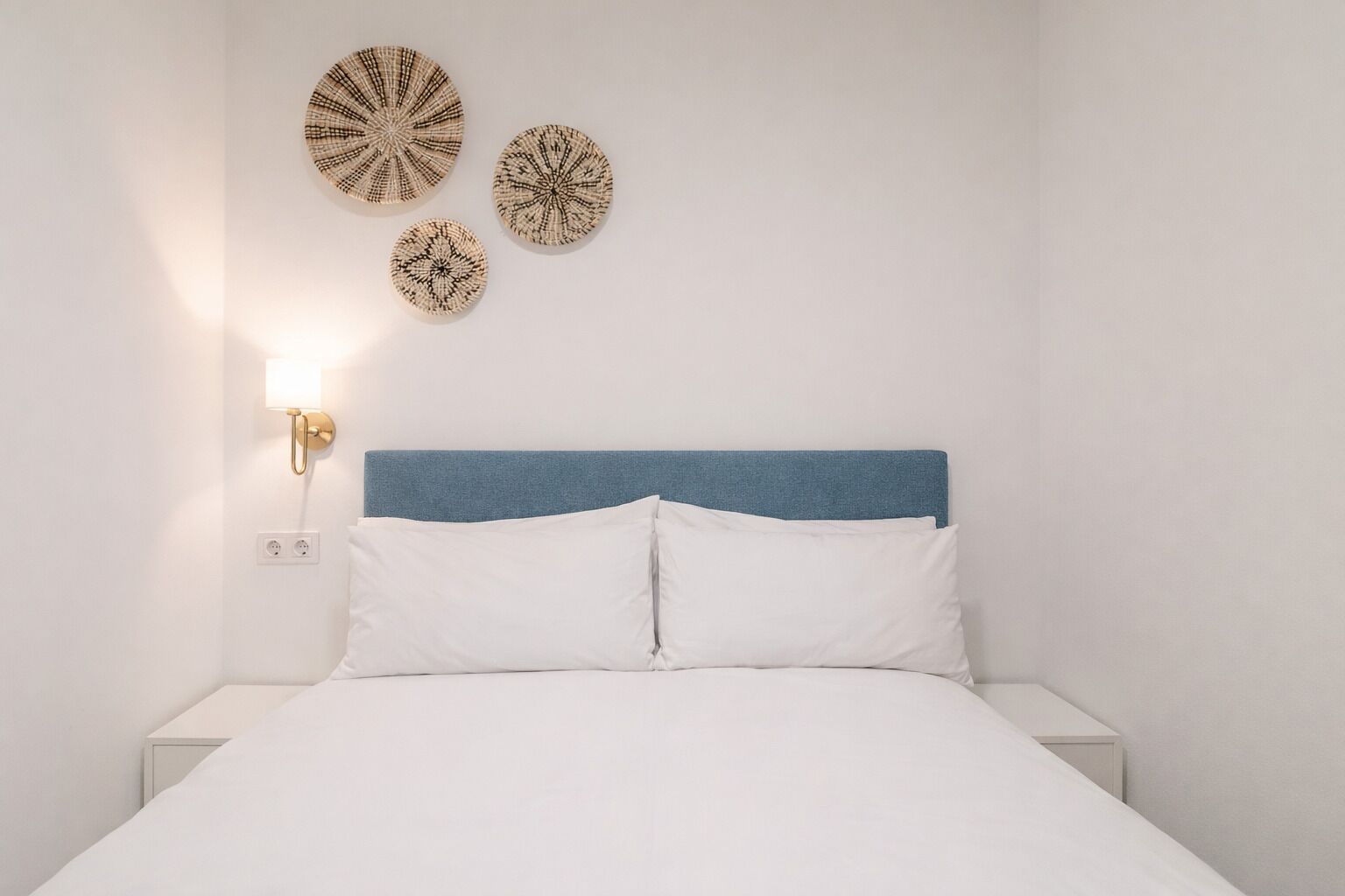 Een slaapkamer met een bed, een blauw hoofdeinde, wit beddengoed en drie decoratieve borden aan de muur.