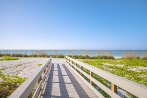 A wooden boardwalk leading to a beach with sand and sea grass.