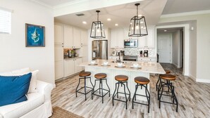 A spacious kitchen with white cabinets, a large island with stools, stainless steel appliances, and pendant lighting. - Changes in Latitude! Gulf Views and Pool! (Bradenton)