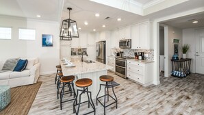A spacious kitchen with white cabinetry, a large island with stools, stainless steel appliances, and a hanging light fixture. - Changes in Latitude! Gulf Views and Pool! (Bradenton)