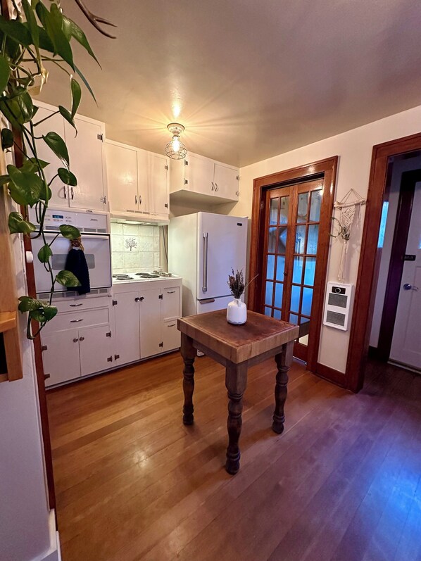 A kitchen with wooden cabinets, a white refrigerator, a wooden table, and a plant.