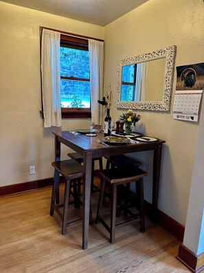 A dining area with a wooden table, chairs, a mirror, a calendar, and a window with curtains.