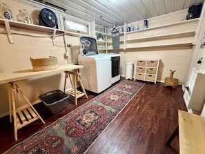 Un cuarto de lavado con lavadora, tendedero, repisas con botellas y un felpudo estampado.