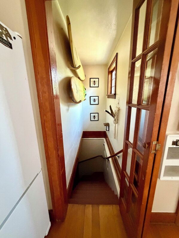 A narrow hallway with a wooden door, a white refrigerator, and a wall-mounted light fixture.