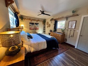 A bedroom with a bed, bedside table, lamp, ceiling fan, and a window with curtains.