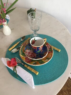 A table set with a floral-patterned plate, a cup, a glass, and a vase with flowers. - Anbê Hospedaria (Porto Seguro)