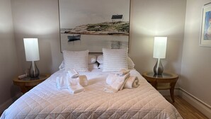 A neatly made bed with a quilted duvet, two bedside tables with lamps, and a large framed picture of a coastal scene on the wall. - West Palm Beach Paradise  (West Palm Beach)