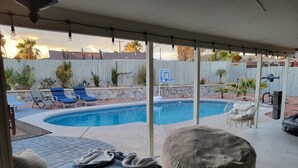 Un patio trasero con piscina, sillas de descanso, una hamaca colgante y un porche cubierto.