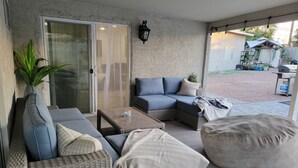 Un patio techado con mobiliario de mimbre, una puerta de vidrio y vista al jardín trasero.